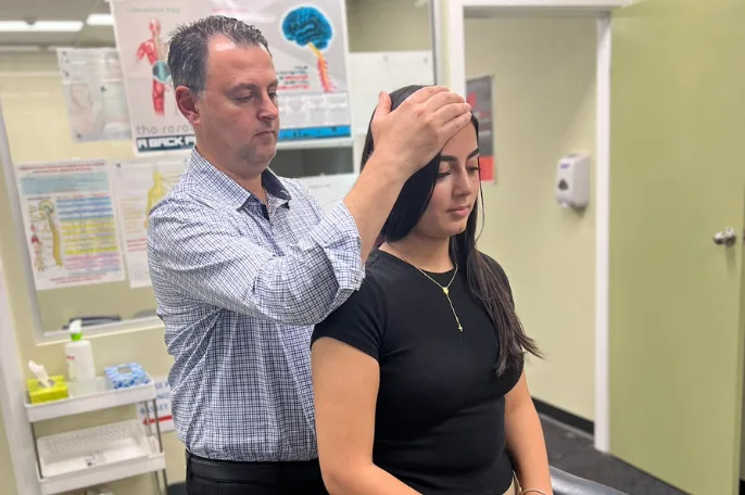 Chiropractor examining a seated patient's head and neck movement at the practice